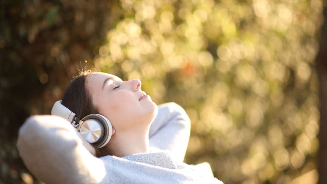 Eine Frau sitzt auf einer Bank, hört Musik und genießt die Sonne.