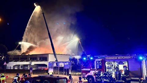 Feuerwehrleute stehen mit ihren Einsatzfahrzeugen vor einer brennenden Lagerhalle in einem Reutlinger Industriegebiet und versuchen diese zu löschen.