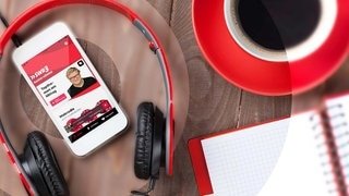 Schreibtisch mit Kopfhörer, Schreibblock und SWR3-Webradio auf dem Smartphone