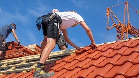 Arbeiter decken ein Ziegeldach in der Pfalz neu ein.