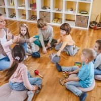 Kindergärtnerin mit auf dem Boden sitzenden Kindern beim Musikunterricht mit verschiedenen Instrumenten und Percussion.