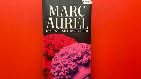 Das Ausstellungsplakat für die Landesausstellung zum römischen Kaiser Marc Aurel in Trier. Kaiserkopf in Rot und Pink.