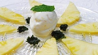 Rezept für ein Dessert: Zitroneneis mit in Rum marinierter Ananas auf einem Glasteller. Auf der Eiskugel in der Mitte liegt ein Minzblatt.