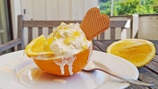 halbe Orange mit Eiscreme darin mit einer Waffel auf einem weißen Teller