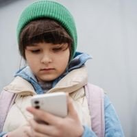 Mädchen steht vor Schulgebäude und scrollt auf dem Smartphone. Nutzung sozialer Medien. Online-Mobbing oder Cybermobbing für junge Schulmädchen.