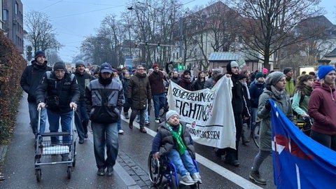 Ein Demonstrationszug gegen die AfD ist auf dem Weg zum Bürgerhaus in Freiburg-Zähringen, wo die AfD am Montagabend eine Wahlkampfveranstaltung abhält. Es nahmen Menschen unterschiedlichen Alters teil. Einer der Teilnehmer sitzt im Rollstuhl, ein anderer ist mit einem Rollator unterwegs. 