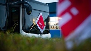 Eine ver.di-Fahne hängt an einem geparkten Linienbus. Beschäftige im privaten Busgewerbe streiken in Baden-Württemberg (Symbolbild).