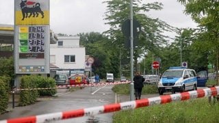 Ein Bereich nahe einer Tankstelle ist mit Absperrband gesichert, im Hintergrund ist ein Polizeiwagen zu sehen.